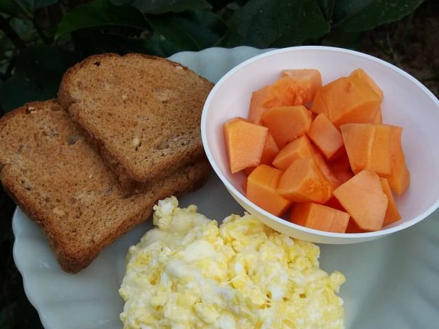 Um pão, ovos mexidos e uma fruta