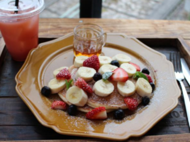 Uma panqueca com muitas frutas e um suquinho de morango.