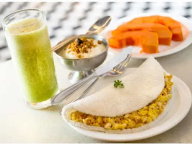 Uma tapioca com ovos mexidos,frutas e um suquinho verde.