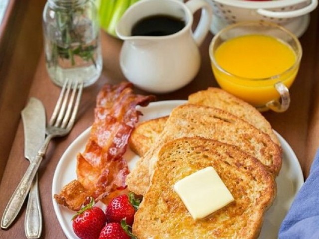 Pão na chapa com queijo do lado bacon e morangos e de bebida um café e um suco natural de laranja