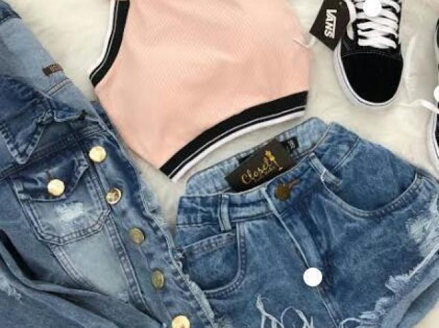 Cropped rosa, jaqueta jeans, short jeans e tênis preto.