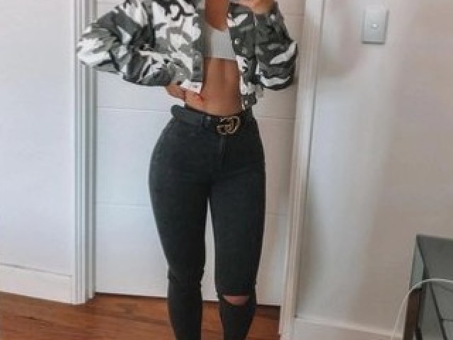 Uma calça jeans preta rasgada no joelho com um top branco e uma jaqueta Bomber camuflada