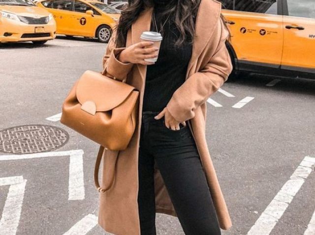 Uma blusa e calça pretas com um sobretudo bege e uma bolsa bege.