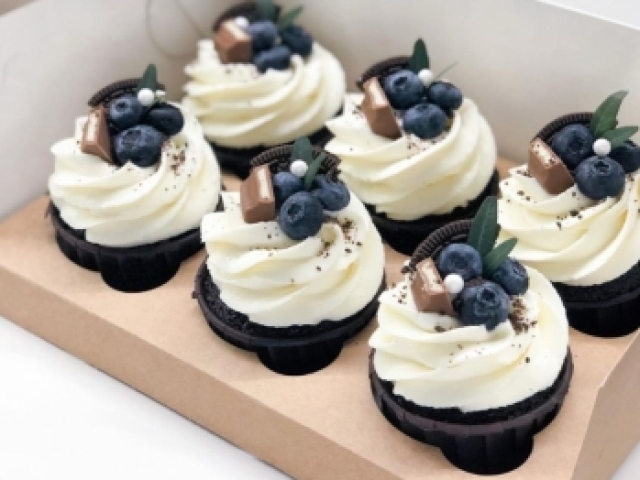 Cupcakes de chocolate com cobertura branca e frutas e doces no topo.