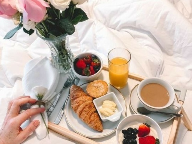 Um grande café da manhã na cama, recheado de croissants, pães, bananas, maçãs, morangos, doces e sucos